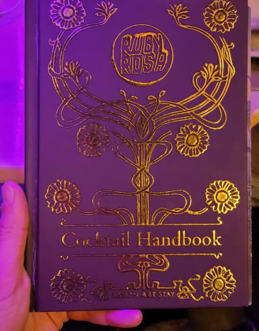 The Ruby Rosa cocktail handbook in gold on deep purple