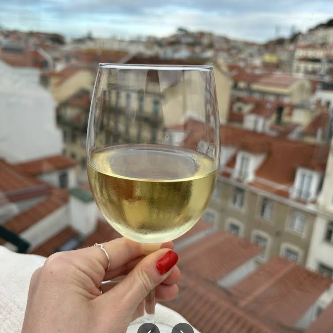 A glass of white wine held above the rooftops of Lisbon